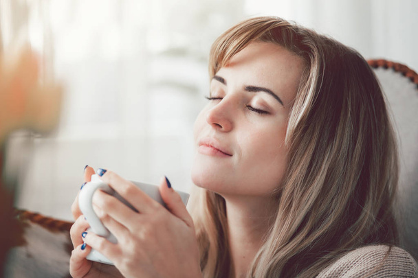 Happy woman in soft sweater relaxing at home with cup of hot tea or coffee, positive emotions - Foto, Imagen
