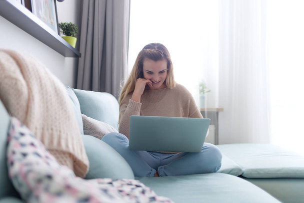 Happy woman at home using laptop sitting on sofa, online working at home - 写真・画像