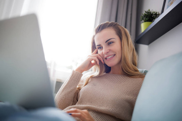 Glückliche Frau zu Hause mit Laptop auf dem Sofa sitzend, online zu Hause arbeitend - Foto, Bild