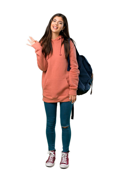 Una toma completa de una adolescente con sudadera y mochila saludando con la mano con expresión feliz
 - Foto, Imagen