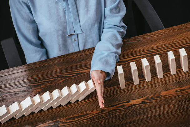 partial view of woman in blue blouse sitting at desk and preventing wooden blocks from falling with hand - Foto, afbeelding