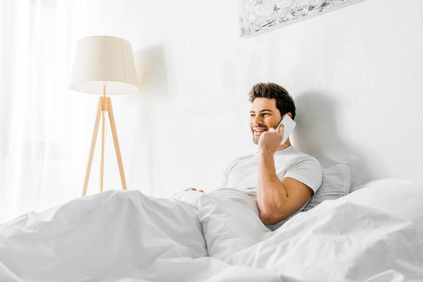 cheerful man talking on smartphone while sitting on bed in the morning - Fotografie, Obrázek