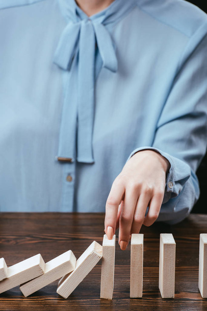 cropped view of woman in blue blouse sitting at desk and preventing wooden blocks from falling - Foto, Imagem