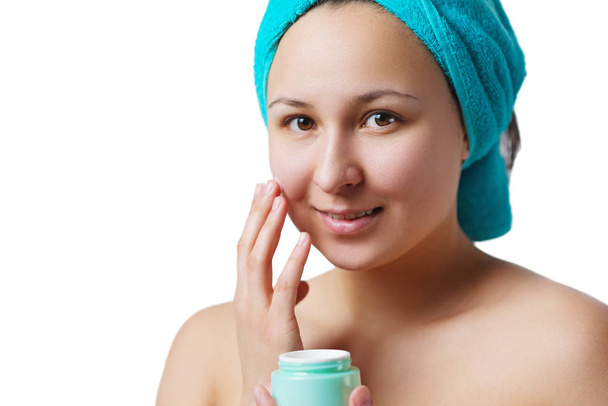 young beautiful girl in a blue turban of towel puts a moisturizer on her face. Isolated - Фото, изображение