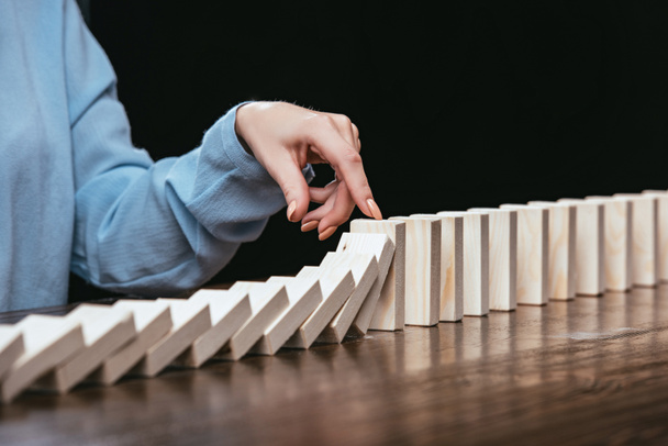 partial view of woman preventing wooden blocks from falling isolated on black - Foto, imagen