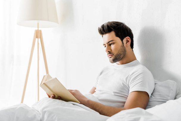 ハンサムな若い男は、朝、ベッドで本を読んで - 写真・画像