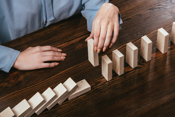partial view of woman picking wooden brick from row of blocks on desk - Foto, Imagen