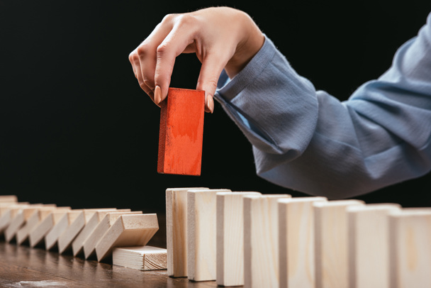 cropped view of woman picking red wooden brick from row of blocks isolated on black - Photo, Image