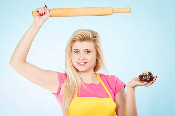 Baking tasty desserts sweets at home concept. Woman holding delicious chocolate cupcake and rolling pin wearing yellow apron. - Photo, Image