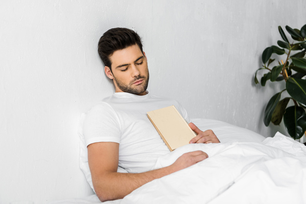 本をベッドで寝ているハンサムな若い男 - 写真・画像