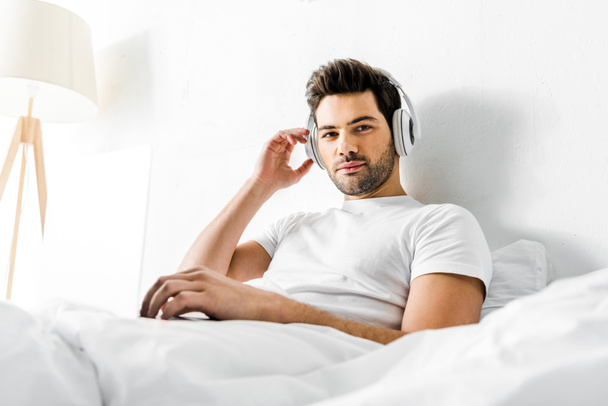 красивий чоловік слухає музику з навушниками та ноутбуком у ліжку
 - Фото, зображення