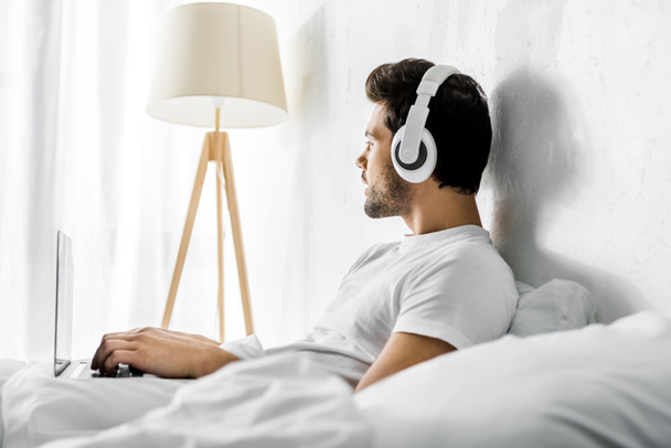 thoughtful man listening music with headphones and laptop in bed - Fotoğraf, Görsel