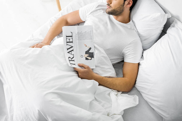 top view of man sleeping in bed with travel newspaper - Foto, Imagem
