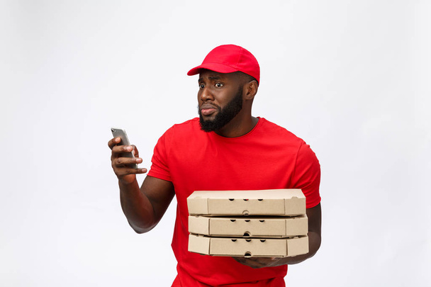 Delivery Concept: Handsome african pizza delivery man talking to mobile with shocking facial expression. Isolated over grey background. - Foto, Bild