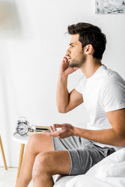 worried man talking on smartphone while sitting on bed in the morning - Foto, Imagem
