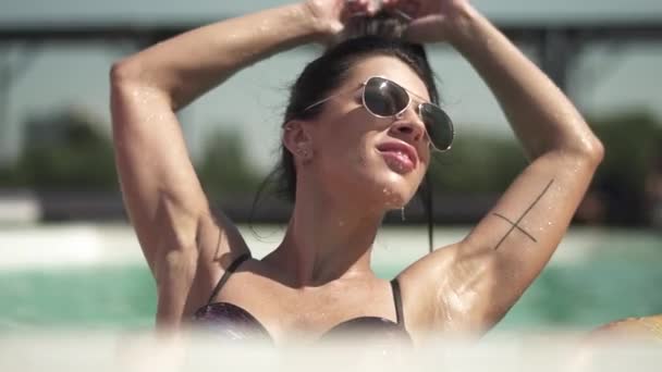 Portrait of beautiful woman in sunglasses swimming in the pool. Leisure of lonely lady in a bikini. - Filmati, video