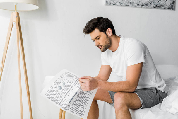 handsome young man reading newspaper in bedroom - Фото, изображение