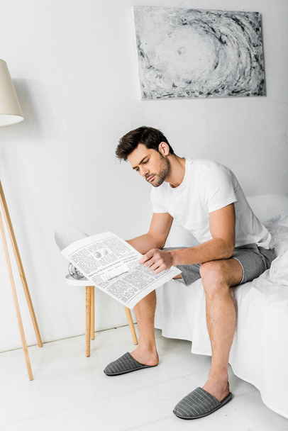 handsome young man in pajamas reading newspaper in bedroom - Foto, Imagem