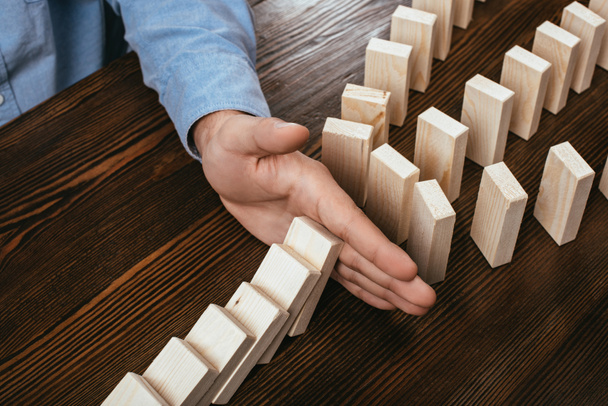 partial view of man preventing wooden blocks from falling on desk - 写真・画像