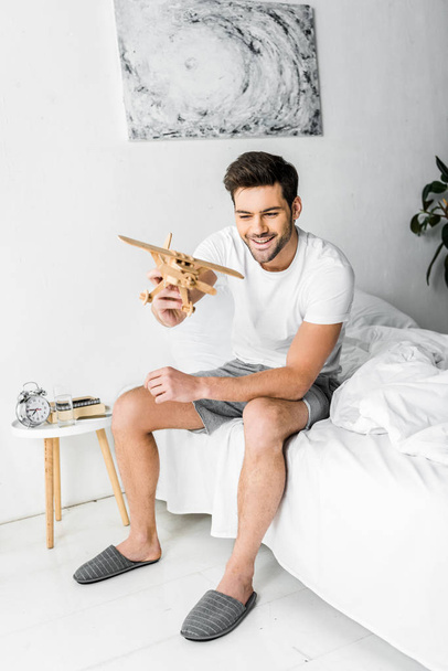 happy man playing with wooden toy plane in bedroom - Foto, imagen