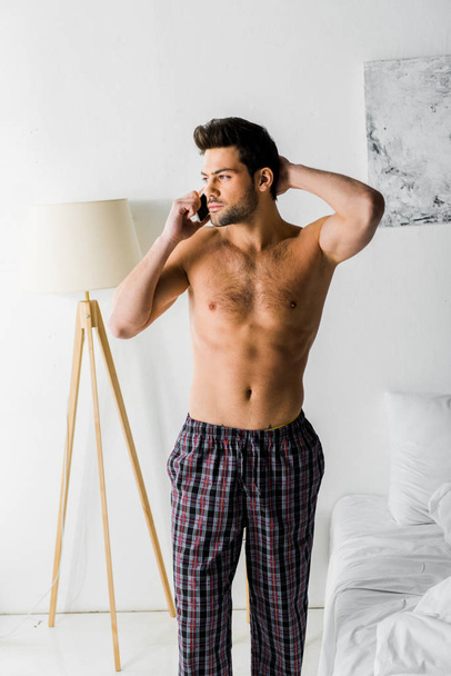 shirtless thoughtful man talking on smartphone in bedroom - Foto, Imagen