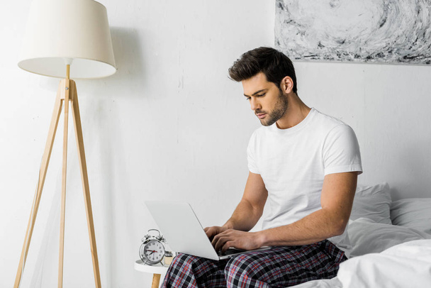 handsome young man using laptop while sitting in bedroom - Foto, Bild