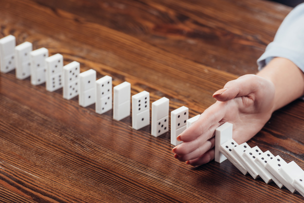 partial view of woman preventing dominoes from falling on wooden desk - Фото, изображение