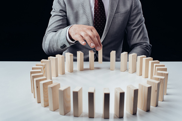 частковий вид людини, що збирає дерев'яну цеглу з ряду блоків на столі ізольовано на чорному
 - Фото, зображення