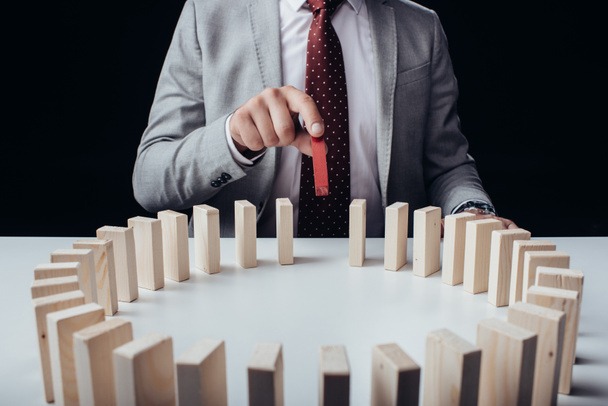 partial view of businessman picking wooden red brick from circle of blocks on desk isolated on black - Photo, Image