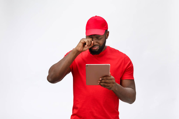 Delivery Concept - Portrait of Serious African American delivery man with tablet in silly aggressive expression and unhappy. Isolated on Grey studio Background. Copy Space - Fotografie, Obrázek