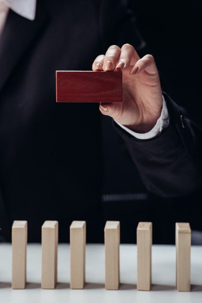 cropped view of woman holding red brick in hand with wooden blocks on foreground isolated on black - Photo, Image