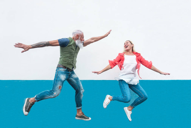 Feliz pareja de ancianos locos saltando juntos al aire libre - Personas maduras de moda divirtiéndose celebrando y bailando al aire libre - Concepto de felicidad, libertad, despreocupación, amor y relación
 - Foto, Imagen
