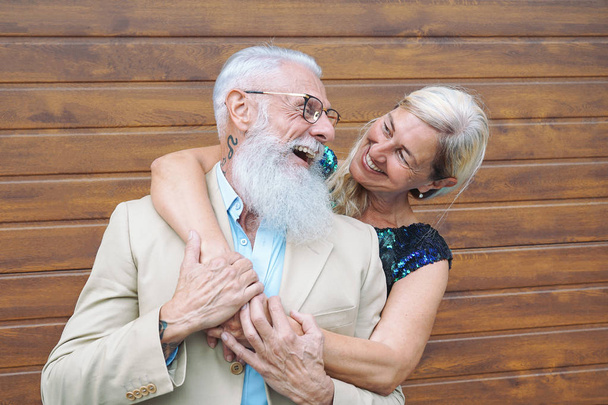 Happy fashion seniors couple embracing outdoor - Mature elegant people laughing and having a tender moment together - Concept of happiness, pensioners, love and relationship - Wooden background - Фото, изображение