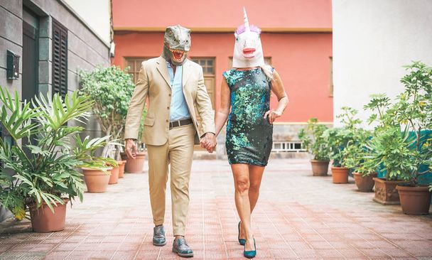 Verrücktes Seniorenpaar mit Dinosaurier- und Einhornmaske - reife Trendleute haben Spaß beim Faschingsumzug - absurdes, exzentrisches, surreales, festliches und lustiges Maskenkonzept - Foto, Bild