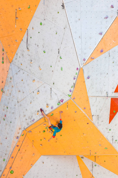 The climber trains on an artificial relief. A woman climbs a climbing route on a street climbing wall. Training in the hall. Strong girl involved in sports. - Photo, Image