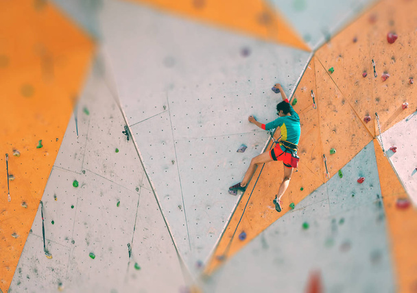 The climber trains on an artificial relief. A woman climbs a climbing route on a street climbing wall. Training in the hall. Strong girl involved in sports. - Foto, Bild