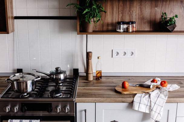 Vaření v moderní kuchyni s ocelovými trouba, nádobí, nůž na dřevěném prkénku s zeleninu, pepř, koření, olej na dřevěnou desku. Domácí jídlo. Stylový kuchyňský nábytek v šedé barvě - Fotografie, Obrázek