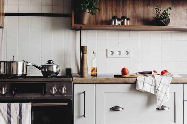 Kochen von Lebensmitteln auf einer modernen Küche mit Stahlherd, Töpfen, Messer auf einem Holzschneidebrett mit Gemüse, Pfeffer, Gewürzen, Öl auf einer Holztischplatte. Essen zu Hause. stilvolle Küchenmöbel in grauer Farbe - Foto, Bild