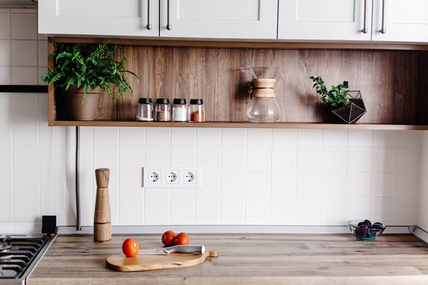 Cooking food on modern kitchen with furniture in grey color and wooden tabletop.  Knife on wooden cutting board with vegetables, pepper, spices. Stylish kitchen interior  in scandinavian style - Photo, Image