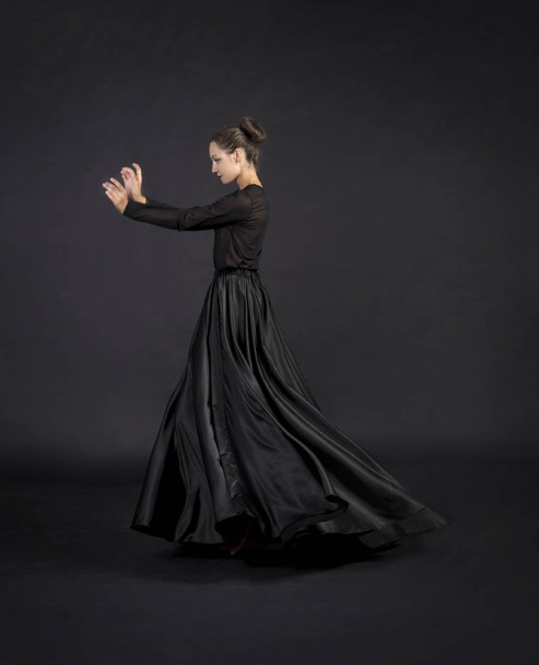Uma jovem garota sorridente de terno preto dançando coreografia moderna.Estúdio filmado em fundo escuro, imagem isolada
. - Foto, Imagem