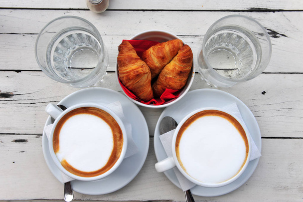 Vista superior de dois cafés, copos de água e croissants na mesa
 - Foto, Imagem
