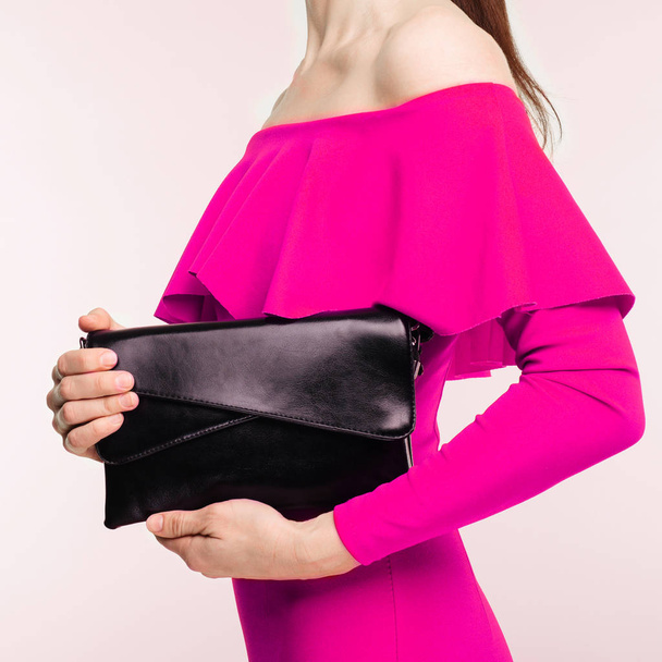 Fashionable woman with a black clutch in her hands and pink evening dress on white background - Photo, image