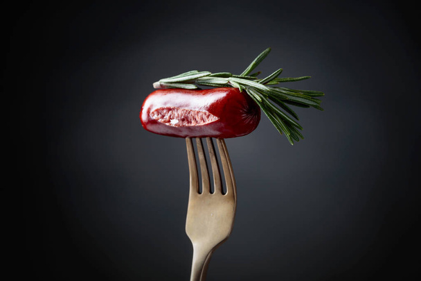 Grilled sausage with rosemary on a fork. Black background, copy space.  - Zdjęcie, obraz