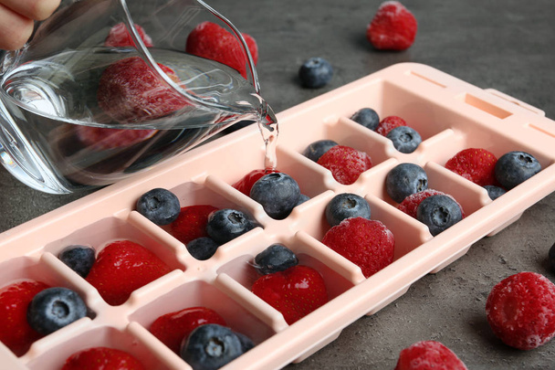 Pouring water into ice cube tray with berries on table, closeup - Foto, imagen