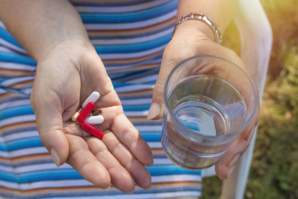 idősebb nő kézzel tabletták és egy pohár vizet - Fotó, kép