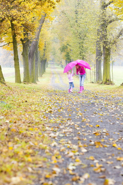 mother and her daughter with umbrellas in autumnal alley - Foto, Imagen