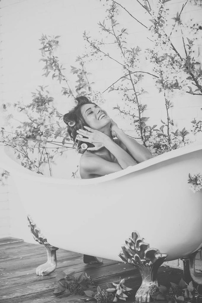 Woman with curlers on hair sit in bath, body care. - Foto, afbeelding