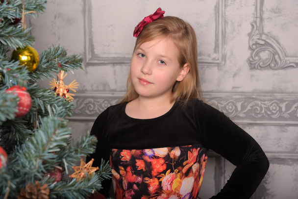 girl blonde child in black with red dress in christmas by the christmas tree alone - Fotó, kép