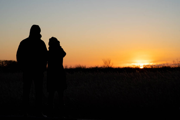 Silhueta de um casal de pé e assistindo o pôr do sol
 - Foto, Imagem