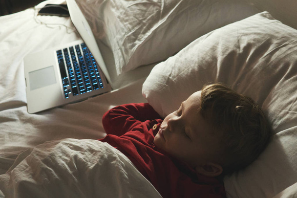 little boy lying and sleeping on the bed with laptop at night. The concept of fatigue from working on a computer. - Valokuva, kuva